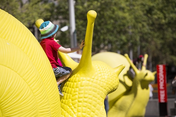 A child sits atop a yellow snail, part of the "Snailovation" project during the Art & About Festival in Sydney, Australia. Photo Courtesy of: City of Sydney.
